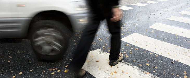 Man on pedestrian crossing in autumn, in danger of being hit by car